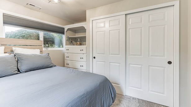 Un dormitorio con cama, ventana, armario y lámpara en el techo.