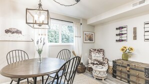 Un comedor con una mesa redonda, sillas, una lámpara colgante, una ventana con cortinas y una estantería de pared para vinos.