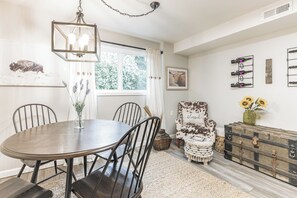 A dining area with a round table, chairs, a hanging light fixture, a window with curtains, and a wall-mounted wine rack. - Peaceful 1-bedroom apartment with private entry in charming Snohomish (Snohomish)