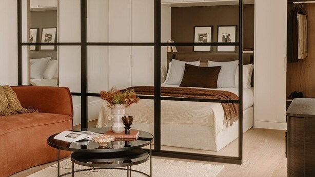 A modern bedroom with a bed, a sofa, a small round table, and a wardrobe. - Fulham Residences Seven (London)