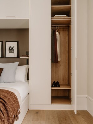 A bedroom with a bed, a closet with hanging clothes, and a shelf with shoes. - Fulham Residences Seven (London)