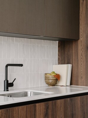 Eine Küche mit einem modernen Wasserhahn, einer weißen Fliesenfassade und Holzschränken.