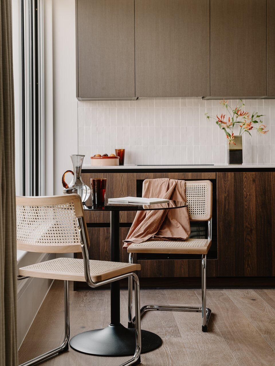 Een moderne keuken met een eethoek, met een houten stoel, een tafel en een vaas met bloemen op het aanrecht.