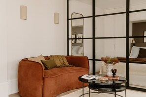 Ein modernes Wohnzimmer mit einem braunen Sofa, einem Glastisch und Blick durch ein großes Fenster.