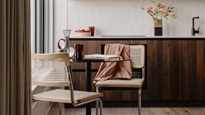 A modern kitchen with wooden cabinets, a dining area with two chairs, and a window with curtains. - Fulham Residences Seven (London)