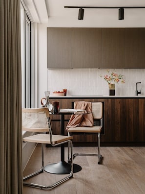 Eine moderne Küche mit Holzausbau, ein Essbereich mit zwei Stühlen und ein Fenster mit Vorhängen.