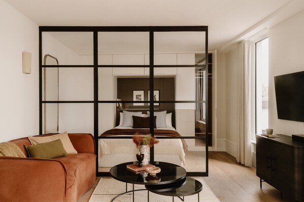 A modern hotel room with a sofa, a round table, a TV, and a large mirror. - Fulham Residences Seven (London)