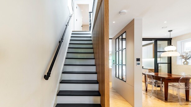 Eine Treppe mit schwarz-weißen Stufen, eine Holzwand und ein Essbereich mit einem Holztisch und Stühlen.