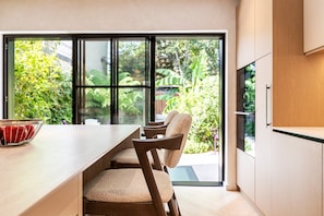 A modern kitchen with a large window, wooden chairs, and a bowl of apples. - Chiswick Four-Bed Garden Retreat (London)