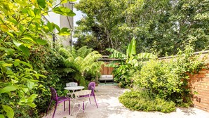 Eine Terrasse im Freien mit Tisch und Stühlen, umgeben von üppiger Vegetation und einem Holzzaun.