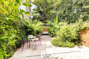 An outdoor patio with a table and chairs, surrounded by lush greenery and a wooden fence. - Chiswick Four-Bed Garden Retreat (London)