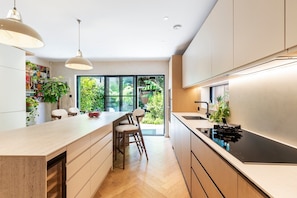 A modern kitchen with a central island, pendant lighting, and a view of a lush garden. - Chiswick Four-Bed Garden Retreat (London)