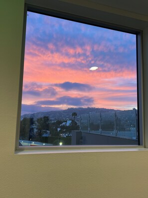 Ein Fenster mit Blick auf einen Sonnenuntergangshimmel, eine Stadtansicht und eine entfernte Hügelkette.