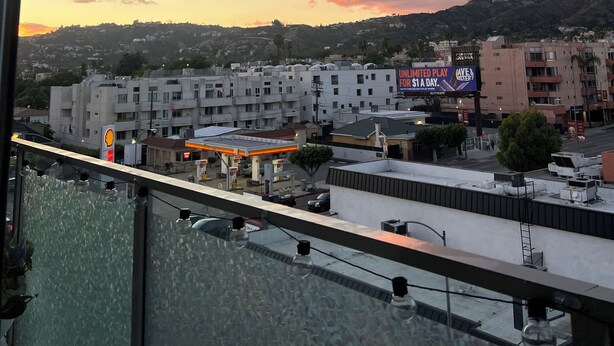 A cityscape with buildings, a Shell gas station, and a billboard advertising unlimited play for $1 a day. - Beautiful 1-bedroom apartment in Hollywood with AC, pool, gym, Hollywood sign (West Hollywood)
