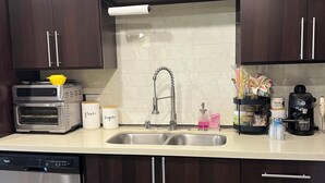 A modern kitchen with dark wood cabinets, a stainless steel dishwasher, a built-in oven, and a sink with a faucet. - Beautiful 1-bedroom apartment in Hollywood with AC, pool, gym, Hollywood sign (West Hollywood)