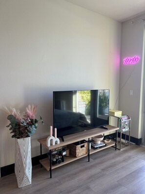 A modern living room with a flat-screen TV on a wooden stand, a potted plant, and a magazine rack. - Beautiful 1-bedroom apartment in Hollywood with AC, pool, gym, Hollywood sign (West Hollywood)