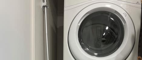Eine gestapelte Waschmaschine und ein Trockner, dazu ein grüner Wischmopp, der an der Wand lehnt.