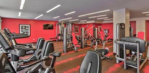 Ein Fitnessstudio mit verschiedenen Trainingsgeräten, darunter Laufbänder, Kraftgeräte und ein rot befloorener Boden.