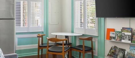 Un espace de vie compact comprenant un coin cuisine, une table ronde avec des chaises et une bibliothèque remplie de livres de voyage.