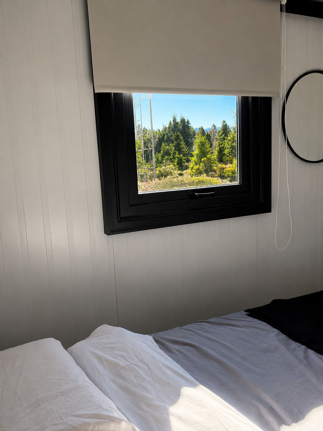 Une chambre à coucher avec un lit, une fenêtre donnant sur des arbres et un objet circulaire accroché au mur.