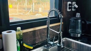 A kitchen with a stainless steel sink, a window with a view of a fence and power lines, and a kettle on the counter. - Modern house with views just steps from Lake Nahuel Huapi (Dina Huapi)