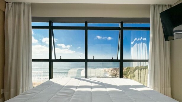 A hotel room with a large bed, a view of the ocean, and a flat-screen TV mounted on the wall. - Blue Sea Hotel Luxury Suite Oceanfront Itapema SC (Itapema)