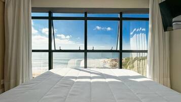 Quarto de hotel com uma cama grande, vista para o oceano e uma televisão de tela plana na parede.