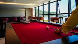 A pool table with a red felt surface, a cue ball, and a person in a yellow shirt preparing to take a shot. - Blue Sea Hotel Luxury Suite Oceanfront Itapema SC (Itapema)