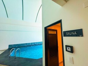 A spa area with a sign for the sauna, a pool with a tiled edge, and a door leading to the sauna. - Blue Sea Hotel Luxury Suite Oceanfront Itapema SC (Itapema)