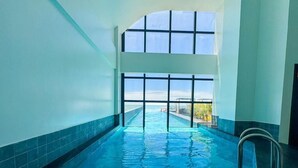 An indoor swimming pool with a view of the sea through large windows. - Blue Sea Hotel Luxury Suite Oceanfront Itapema SC (Itapema)