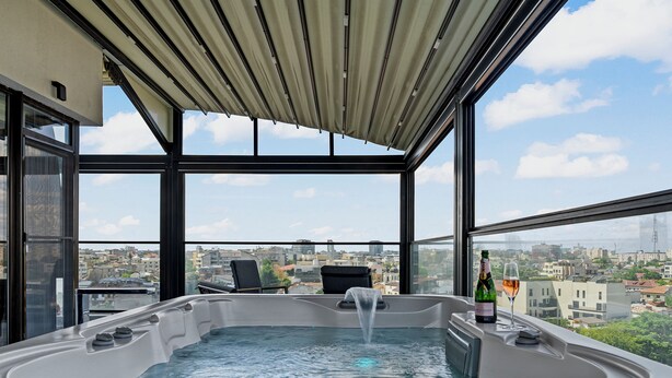 A hot tub with a city view, a bottle of champagne, and a glass on a balcony.