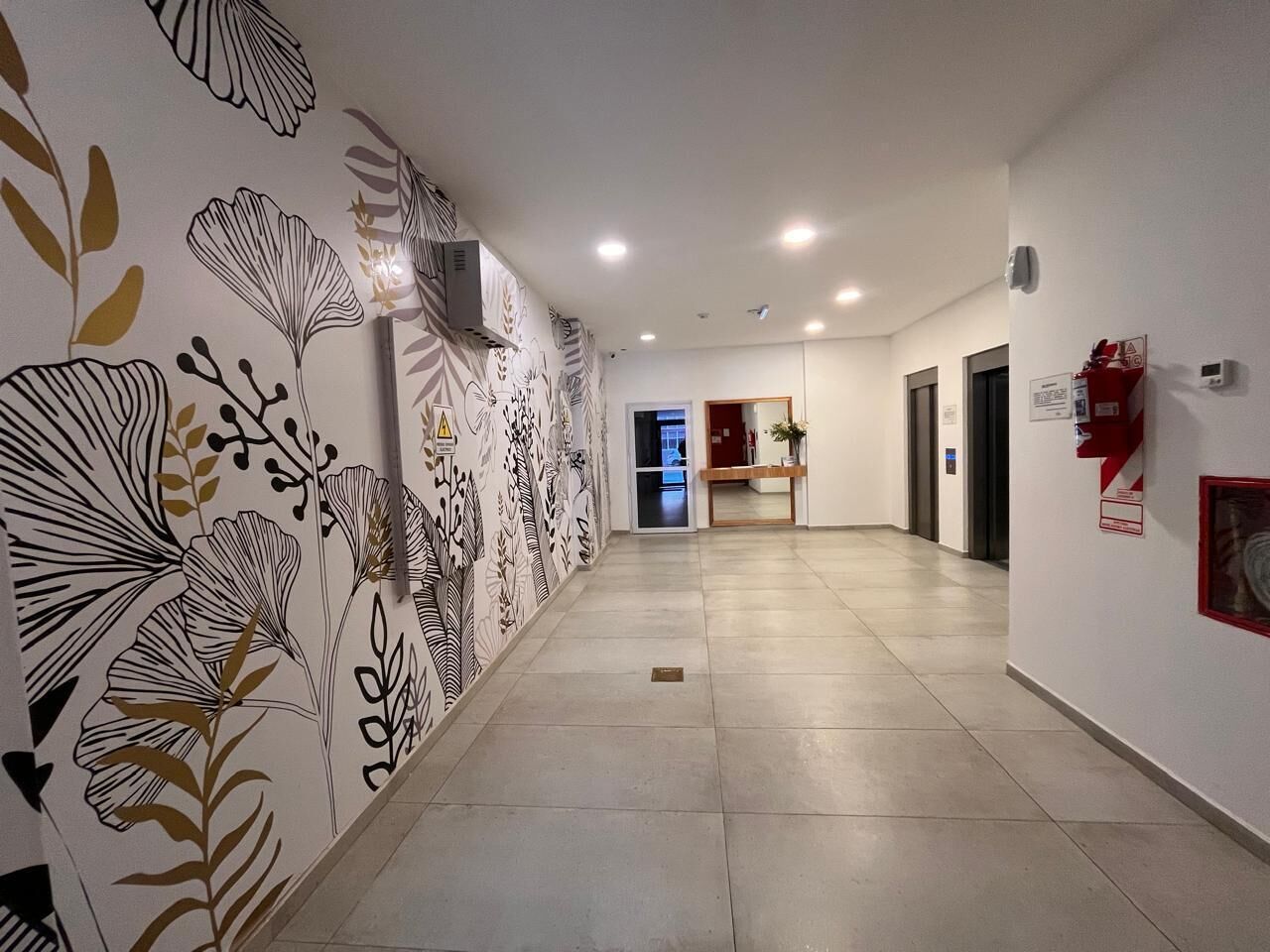 Un pasillo con detalles decorativos en la pared, un extintor y una puerta al final.