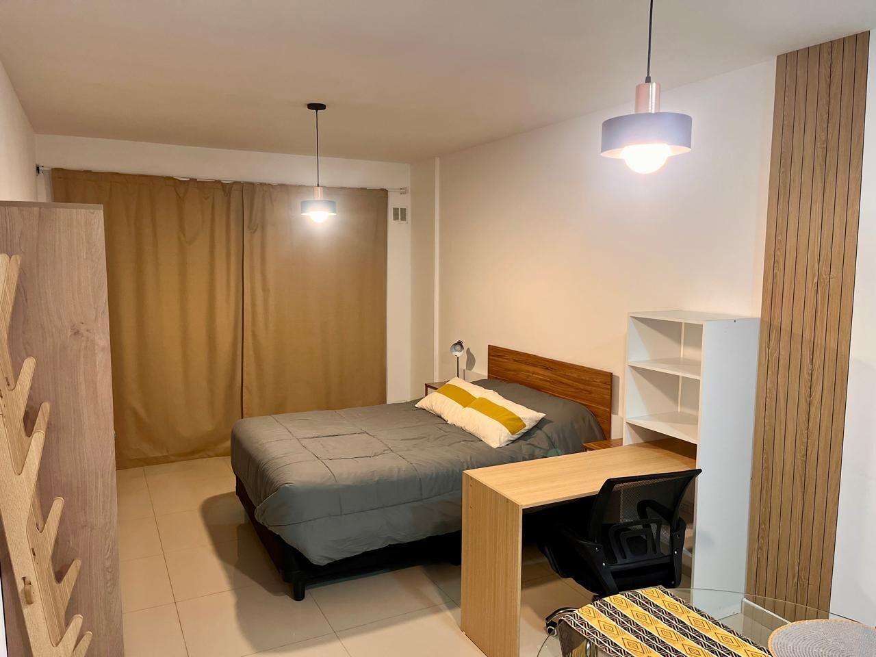 A bedroom with a bed, desk, chair, and two pendant lights.