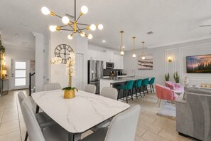 A modern kitchen with white cabinets, a stainless steel refrigerator, and a dining area with a marble table and chairs. - 4 BD/ 3 BA/ Storey Lake (4383 SL) (Kissimmee)