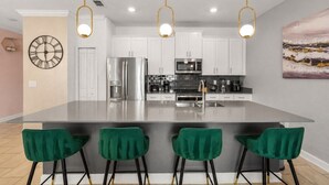 Une cuisine moderne dotée d’un îlot central, d’appareils électroménagers en acier inoxydable et de tabourets de bar verts.