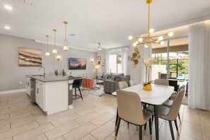 Eine moderne Küche mit einer zentralen Kochinsel, ein Essbereich mit weißem Tisch und Stühlen sowie ein Wohnzimmer mit grauem Sofa.