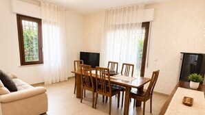 Un salon moderne avec un canapé, une table à manger et des chaises. Il y a un téléviseur accroché au mur et une plante posée sur la table d’appoint.