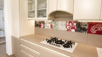 A modern kitchen with beige cabinetry, a gas stove, and a backsplash with floral patterns.