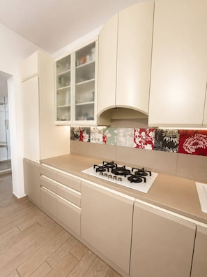 A modern kitchen with beige cabinetry, a gas stove, and a backsplash with floral patterns.
