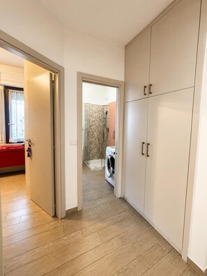 A hallway with a washing machine, a red cabinet, and a wardrobe.