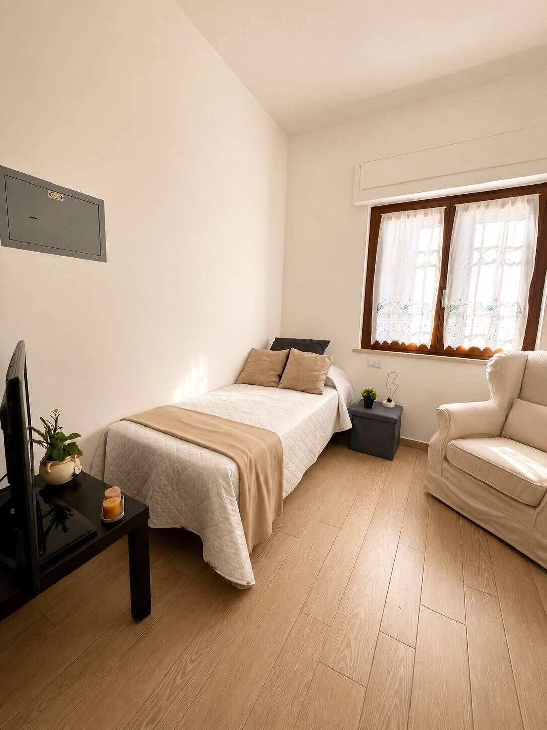 Ein Schlafzimmer mit Bett, Nachttisch, Fernseher und einem Fenster mit Vorhängen.