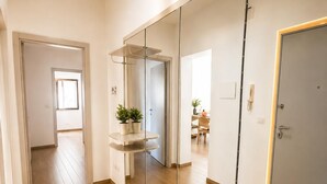Un couloir doté d’un plancher en bois, d’un mur recouvert de miroirs et d’une porte donnant sur une pièce où se trouvent une table et des chaises.