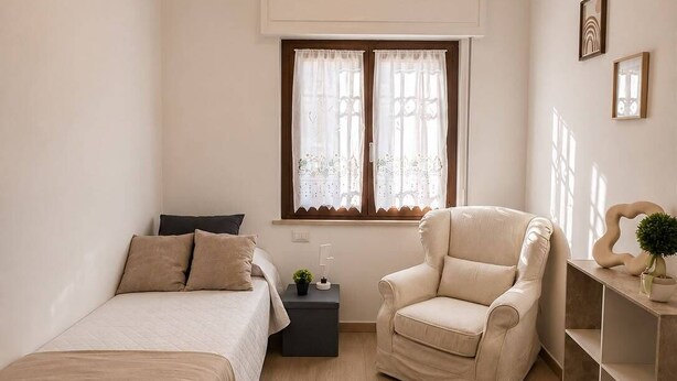 Une chambre à coucher minimaliste avec deux lits, une chaise, une table de chevet et une fenêtre avec des rideaux.
