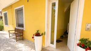 Un bâtiment jaune avec un banc, des plantes en pot et une entrée carrelée.