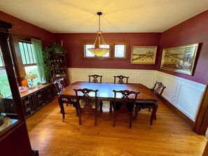 A dining room with a wooden table and chairs, a chandelier, and artwork on the walls.