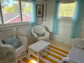 Ett rum med möbler i rotting, ett randigt golv och fönster med gardiner.