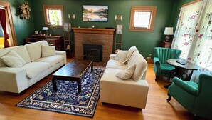 Una sala de estar con chimenea, dos sofás, una mesa de centro y un sillón verde.