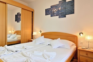 A hotel room with a large bed, a wooden headboard, a nightstand with a lamp, a wall-mounted artwork, and a mirror. - Bošković-Apartment-2, Modern Family Apartment with Balconies | 2 Bedrooms 6 pers (Rudina)