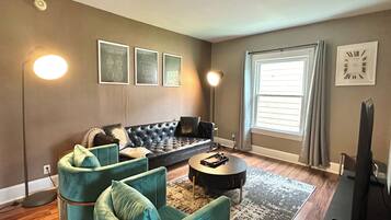 Ein Wohnzimmer mit einem Ecksofa, zwei Sesseln, einem Couchtisch und einem Flachbildfernseher.