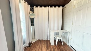A room with a wooden floor, white curtains, a white desk, and a white chair.